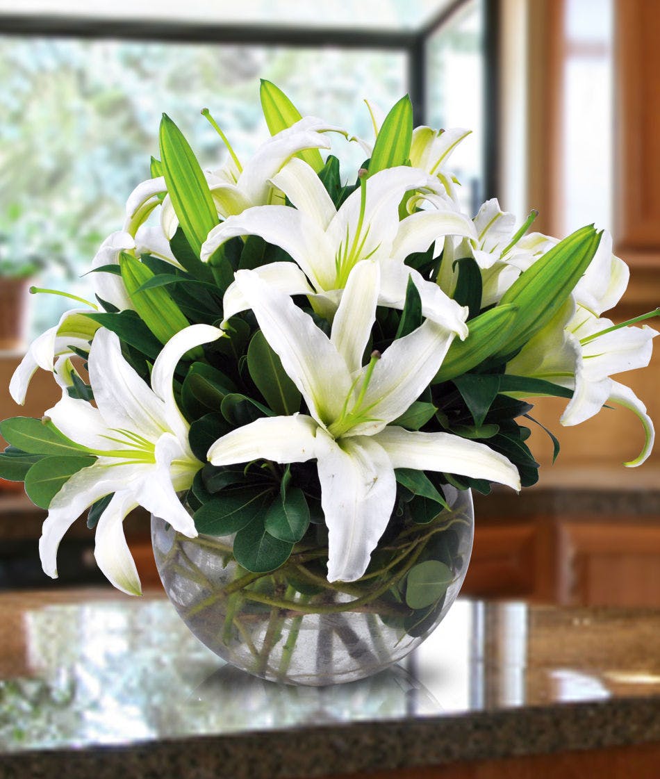 White lilies and greenery in a clear glass bowl vase.