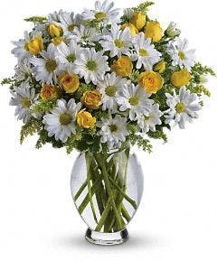 White daisies and yellow spray roses in a clear glass vase.
